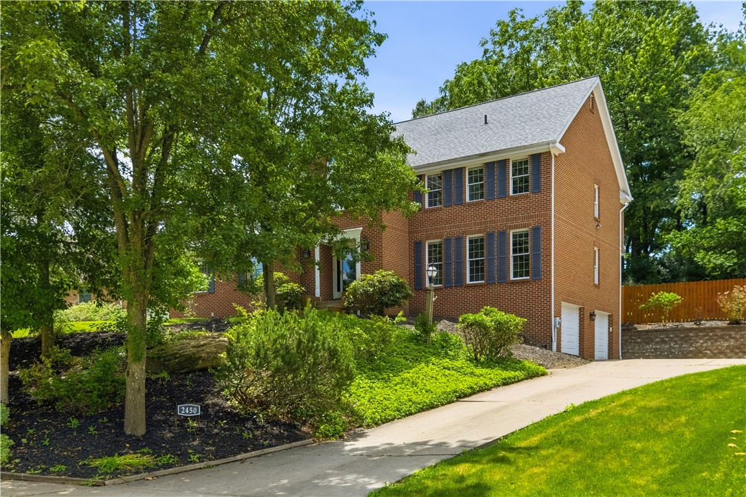 Two-story brick house with dark shutters and a curved driveway, framed by mature trees and landscaping.