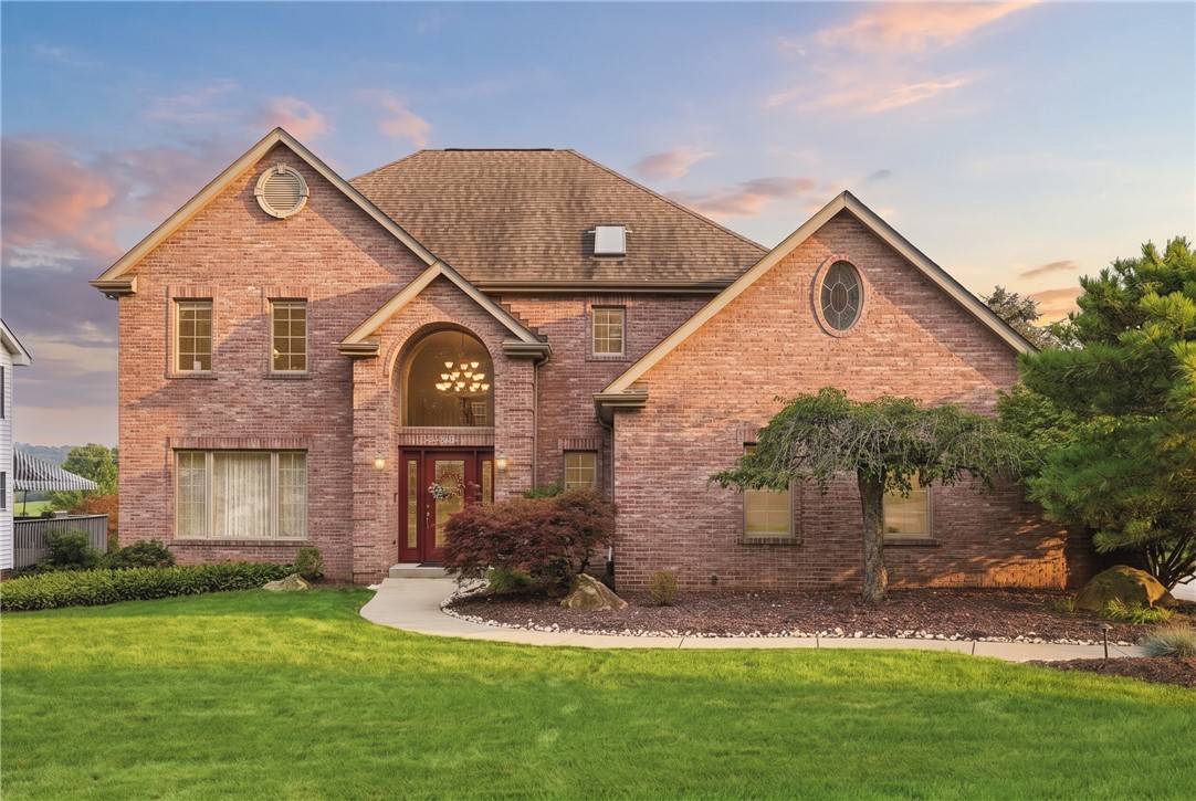 Two-story brick home with an arched entry and landscaped front lawn in warm evening light.