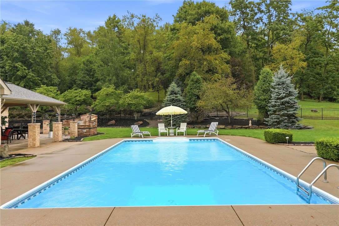 Outdoor swimming pool with a covered stone pavilion, lounge chairs, and wooded landscaping.
