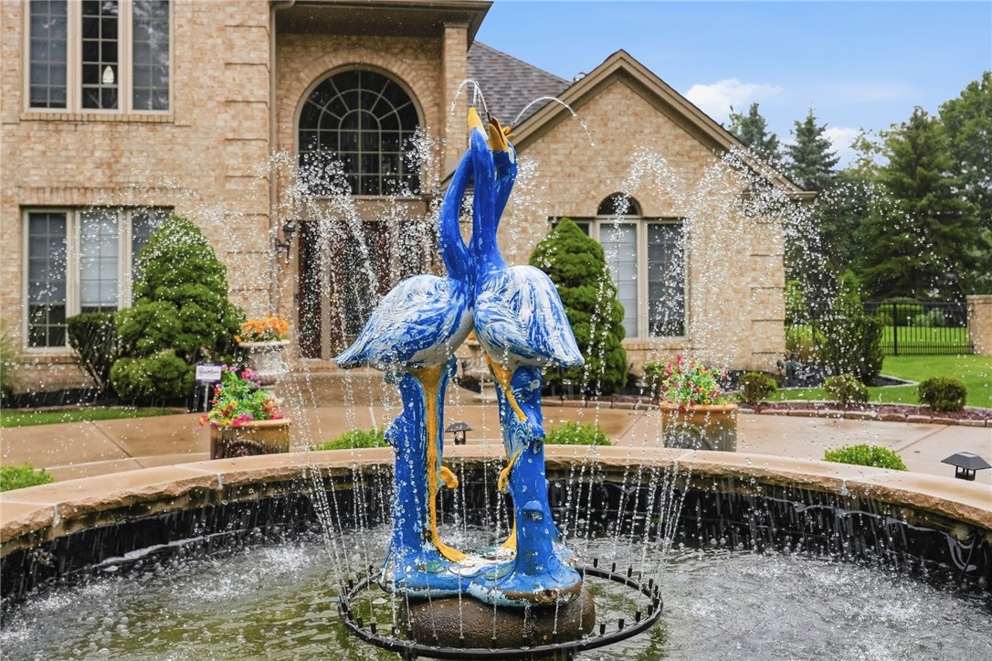 Stone two-story home behind a courtyard fountain with blue bird sculptures.