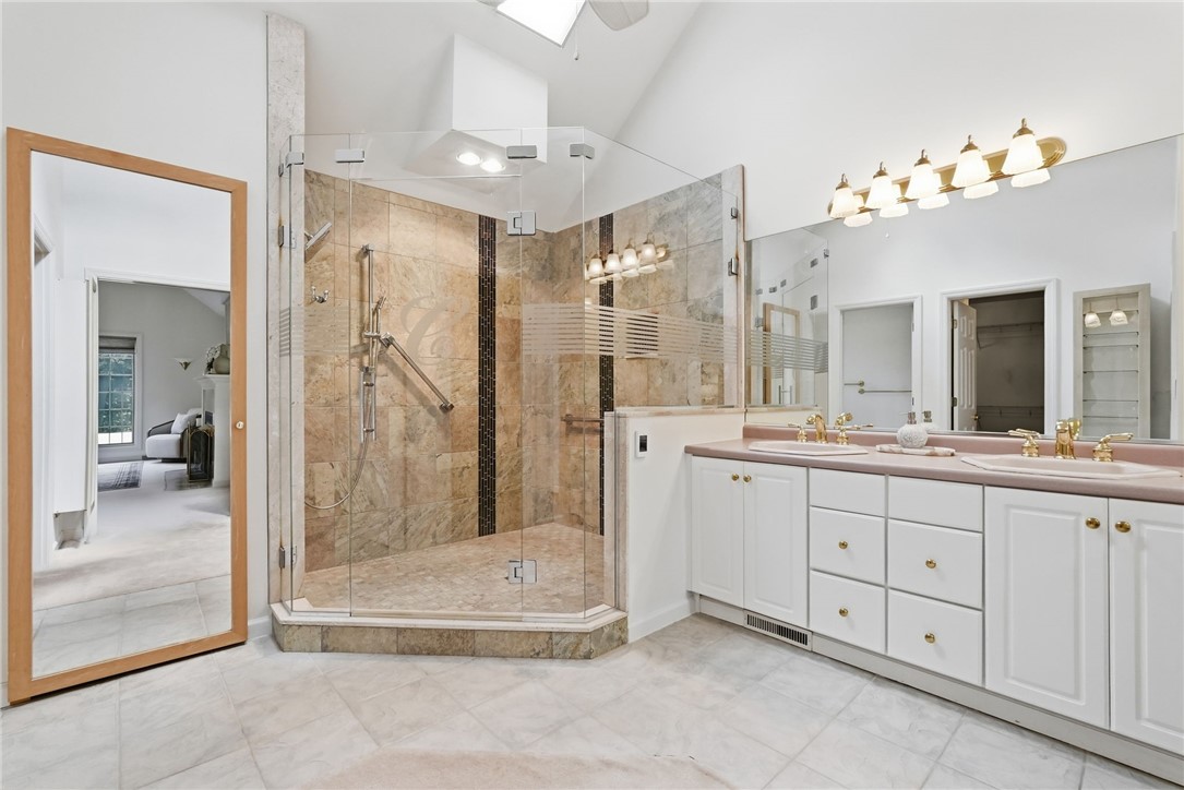 Bathroom with a stone-tiled corner shower and long double vanity with pink countertops.