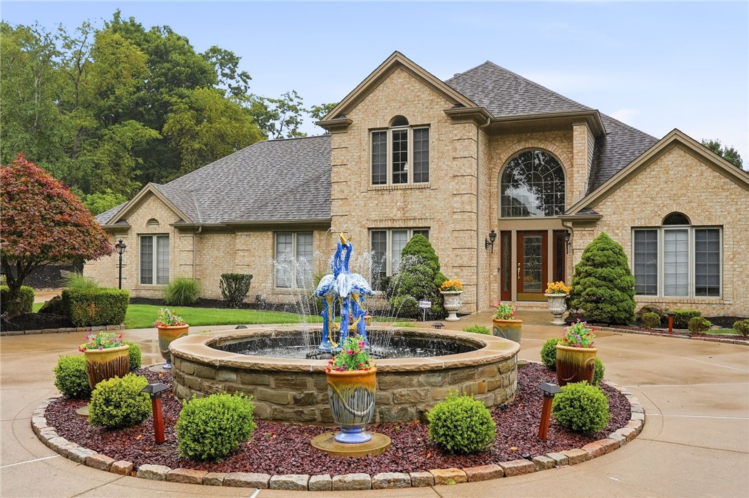 Tan stone house with a circular fountain and landscaped front courtyard.