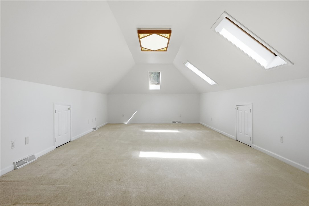 Vacant attic room with beige carpet, sloped ceiling, and several skylights.