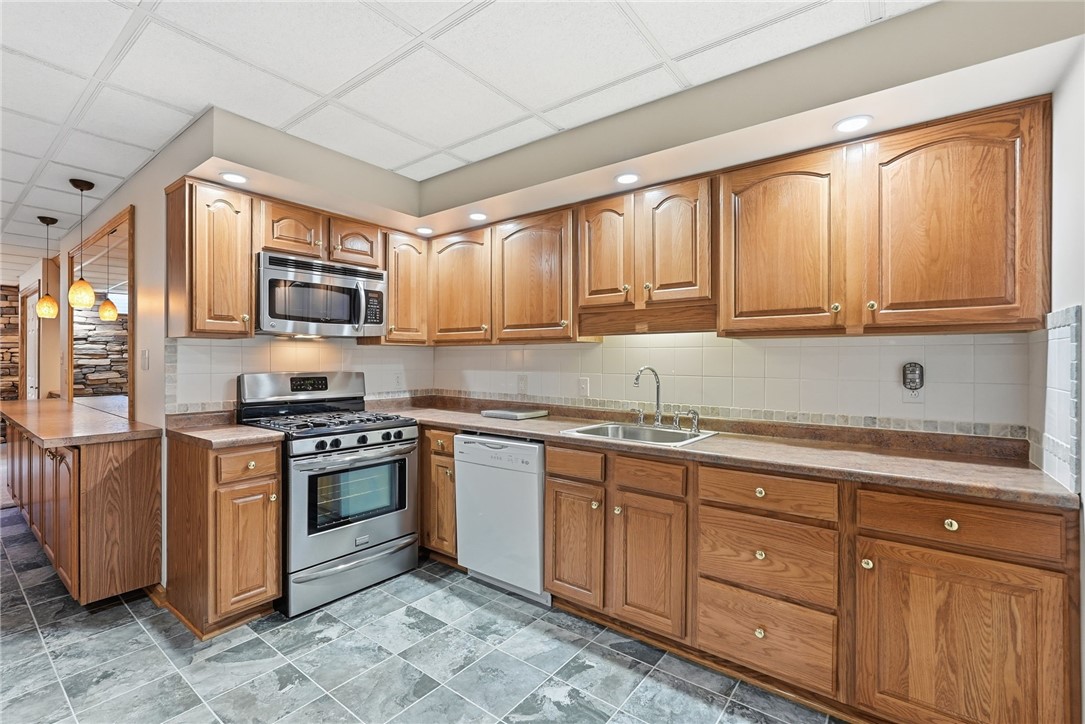 Kitchen with honey-toned wood cabinets, stainless steel appliances, and gray tile flooring.