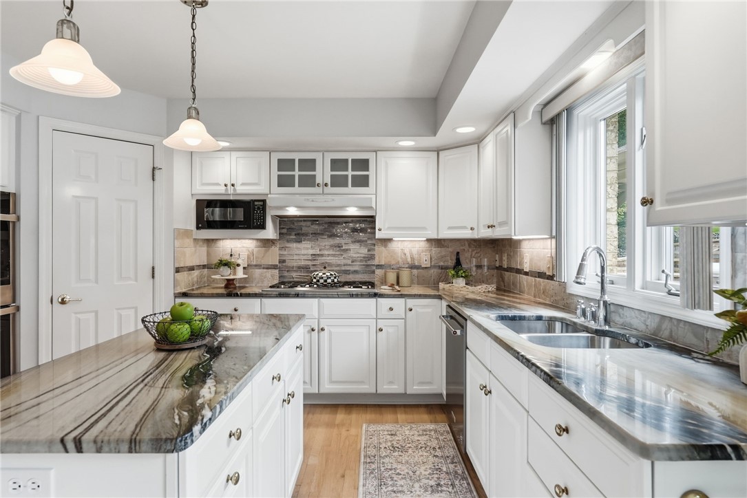 Kitchen with white cabinets, veined marble counters, a central island, and a double sink beneath large windows.