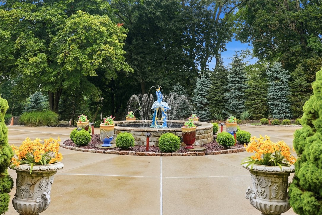 Landscaped courtyard with a circular stone fountain, blue sculpture, flower urns, and mature trees.