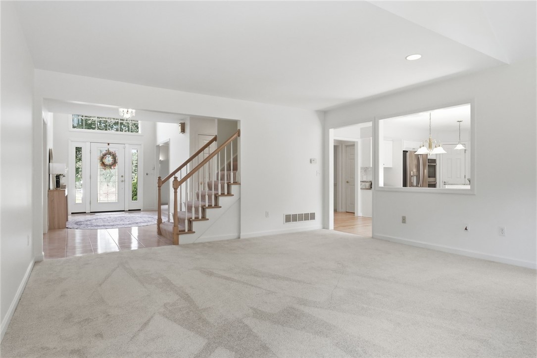 Mostly empty living room with light carpet, open entry foyer, staircase, and kitchen pass-through.