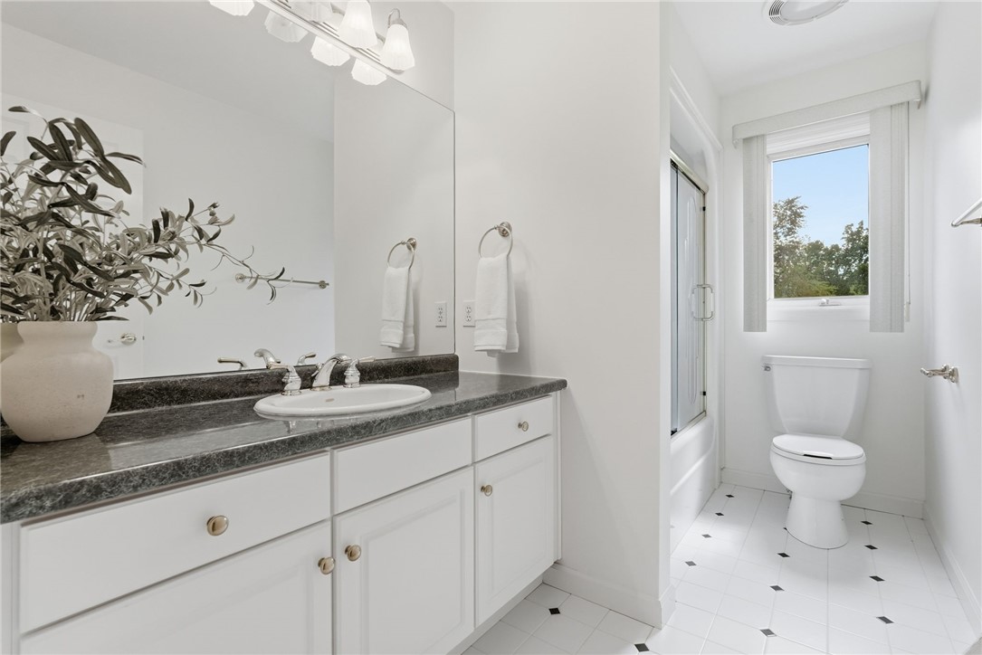 Bathroom with a dark stone vanity, large mirror, and separate toilet area beside a window.