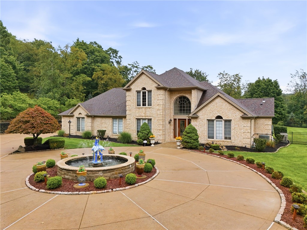 Two-story stone house with a circular driveway, landscaped fountain, and mature trees.