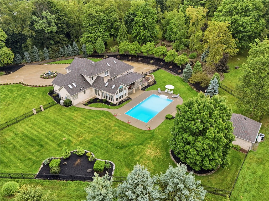 Aerial view of a home with a swimming pool, expansive lawn, and mature trees.