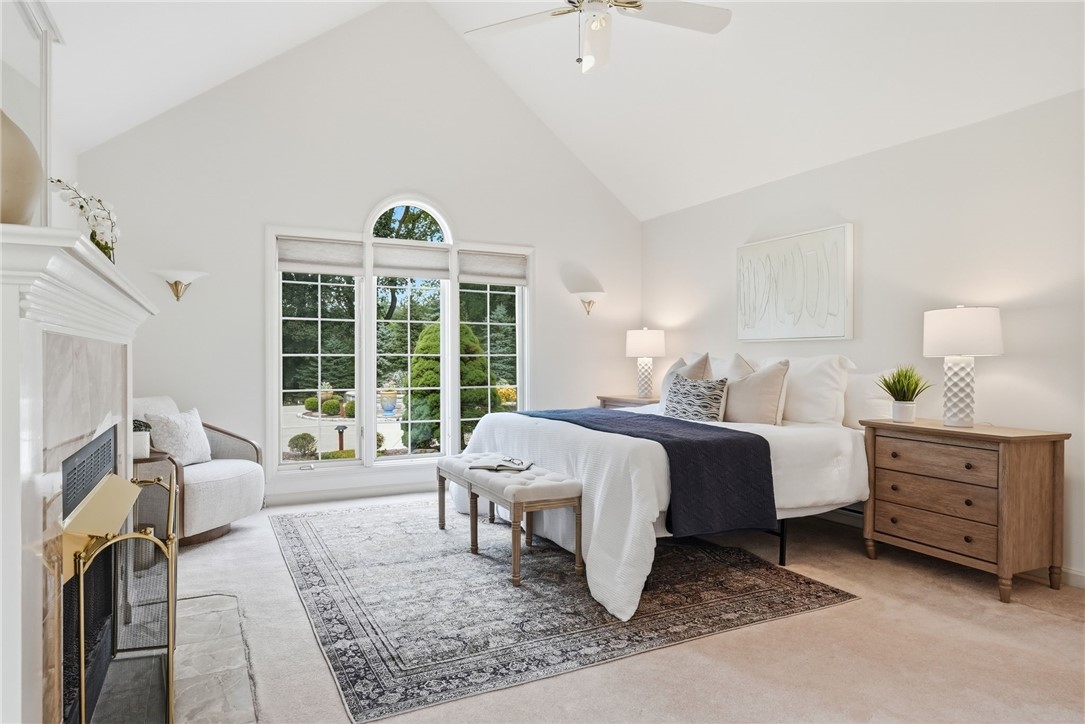 Staged bedroom with a vaulted ceiling, fireplace, and arched garden-view window.
