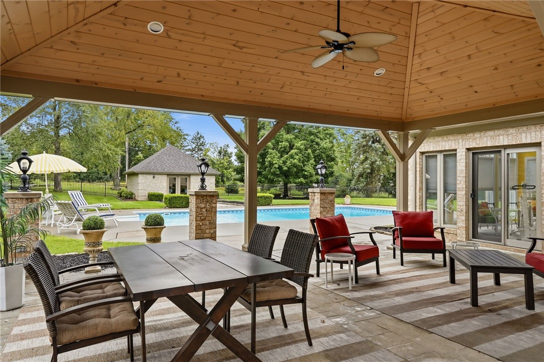 Covered patio with outdoor dining and seating overlooking a swimming pool and stone pavilion.