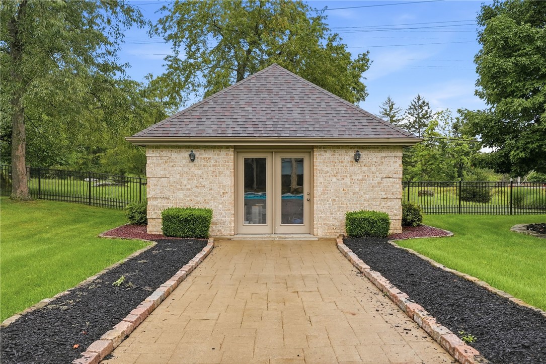 Detached brick building with a hipped roof at the end of a paved walkway, surrounded by lawn and fencing.