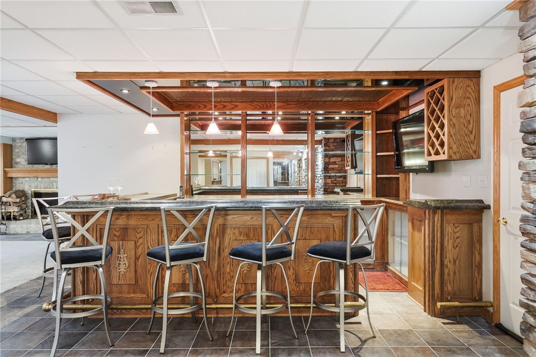 Home bar with wood-paneled counter, four stools, mirrored shelves, and an adjoining fireplace area.