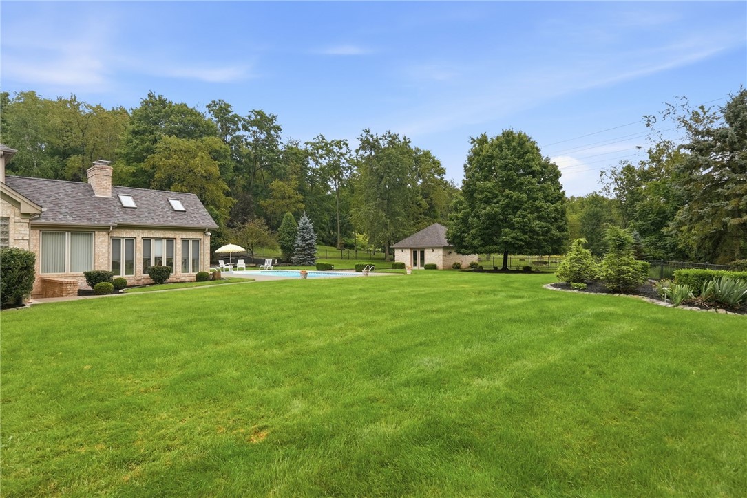 Backyard with a swimming pool, broad lawn, patio seating, and detached outbuilding.
