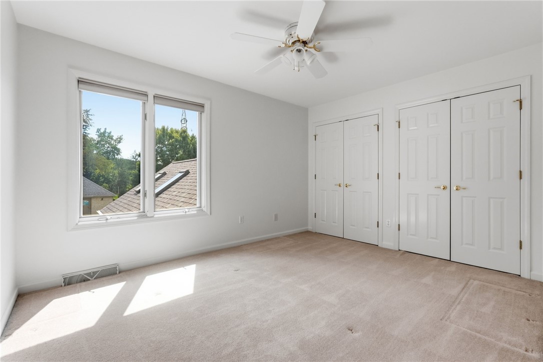 Empty carpeted bedroom with a ceiling fan, two windows, and double-door closets.