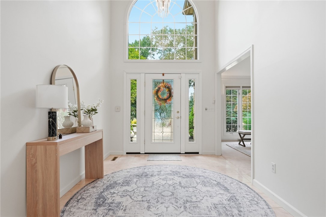 Bright foyer with a decorative glass front door, tall arched window, and round rug.
