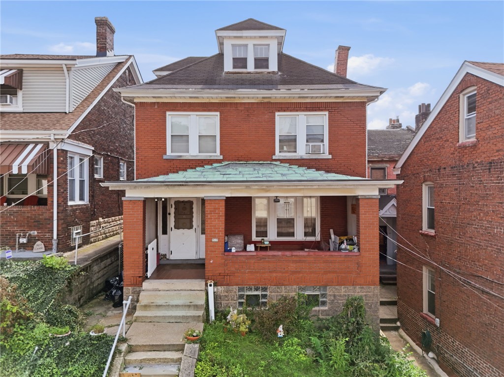 Red brick home with a covered front porch, concrete steps, and a dormer window.