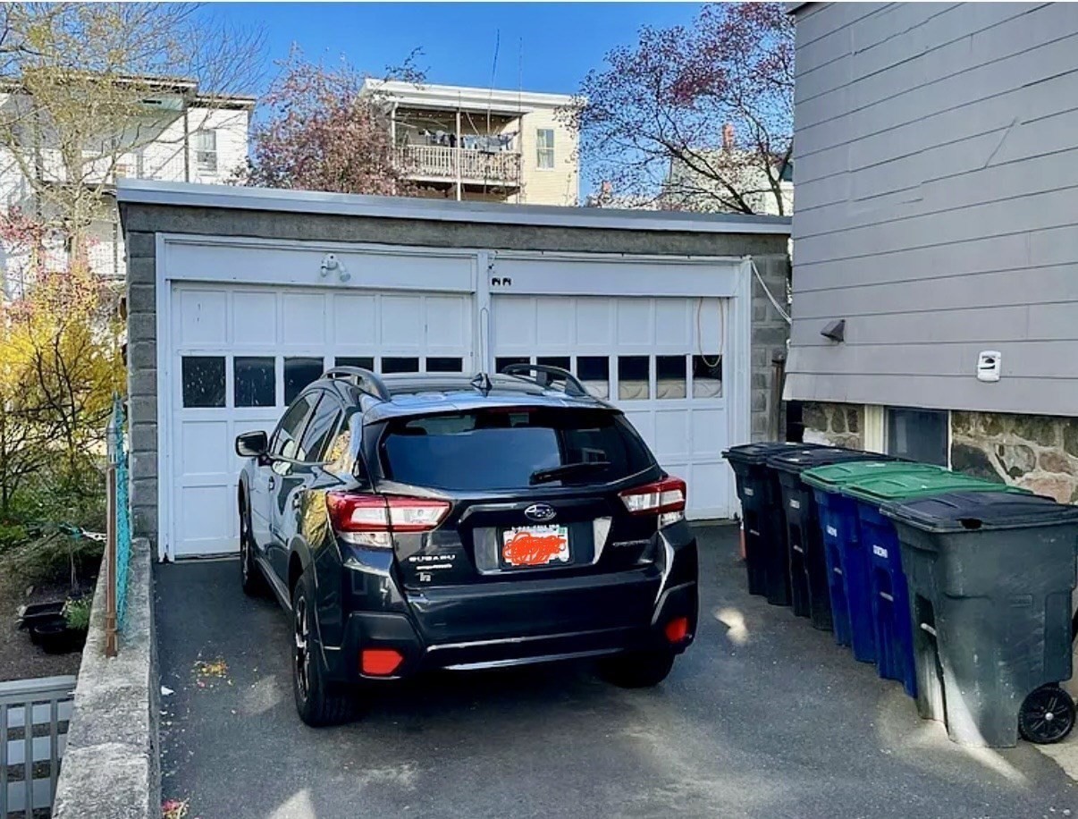 Two-door garage with a Subaru parked in the driveway and bins along the side.