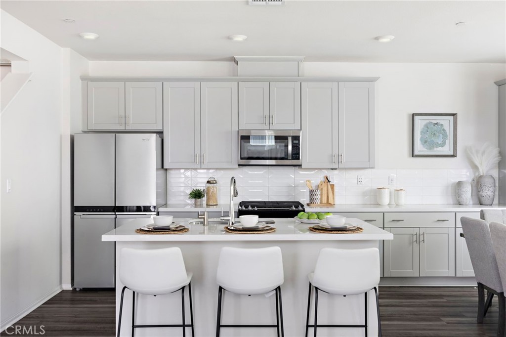Bright kitchen with gray cabinetry, stainless appliances, and a white island with three stools.