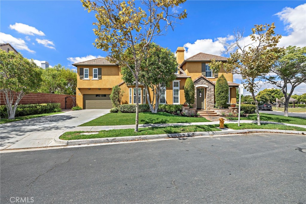 Two-story tan stucco house with a stone entry, attached garage, and landscaped front yard.