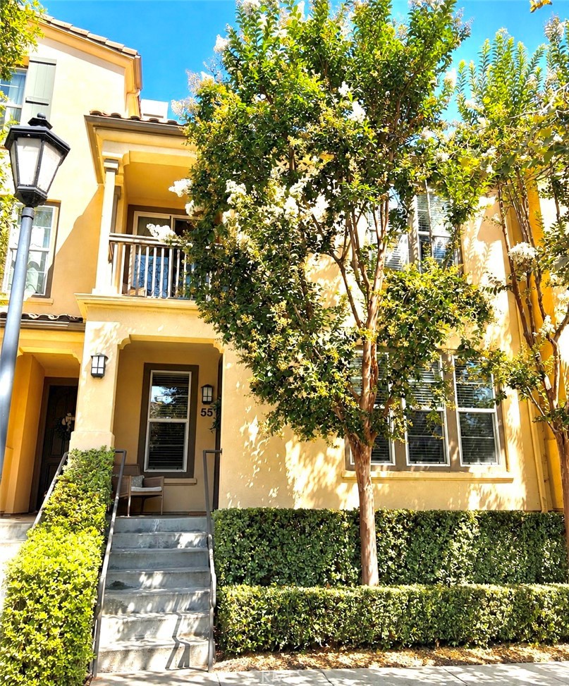 Yellow multi-story home with front steps, a small balcony, and trees shading the facade.