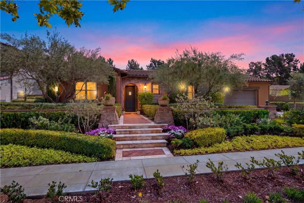 Single-story stucco home with a landscaped stone entry beneath a pink dusk sky.
