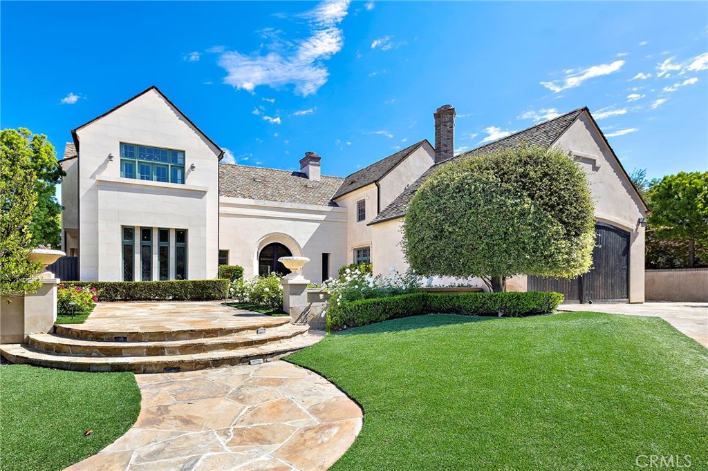 Large stucco home with a curved stone walkway, landscaped lawn, and dark arched garage door.