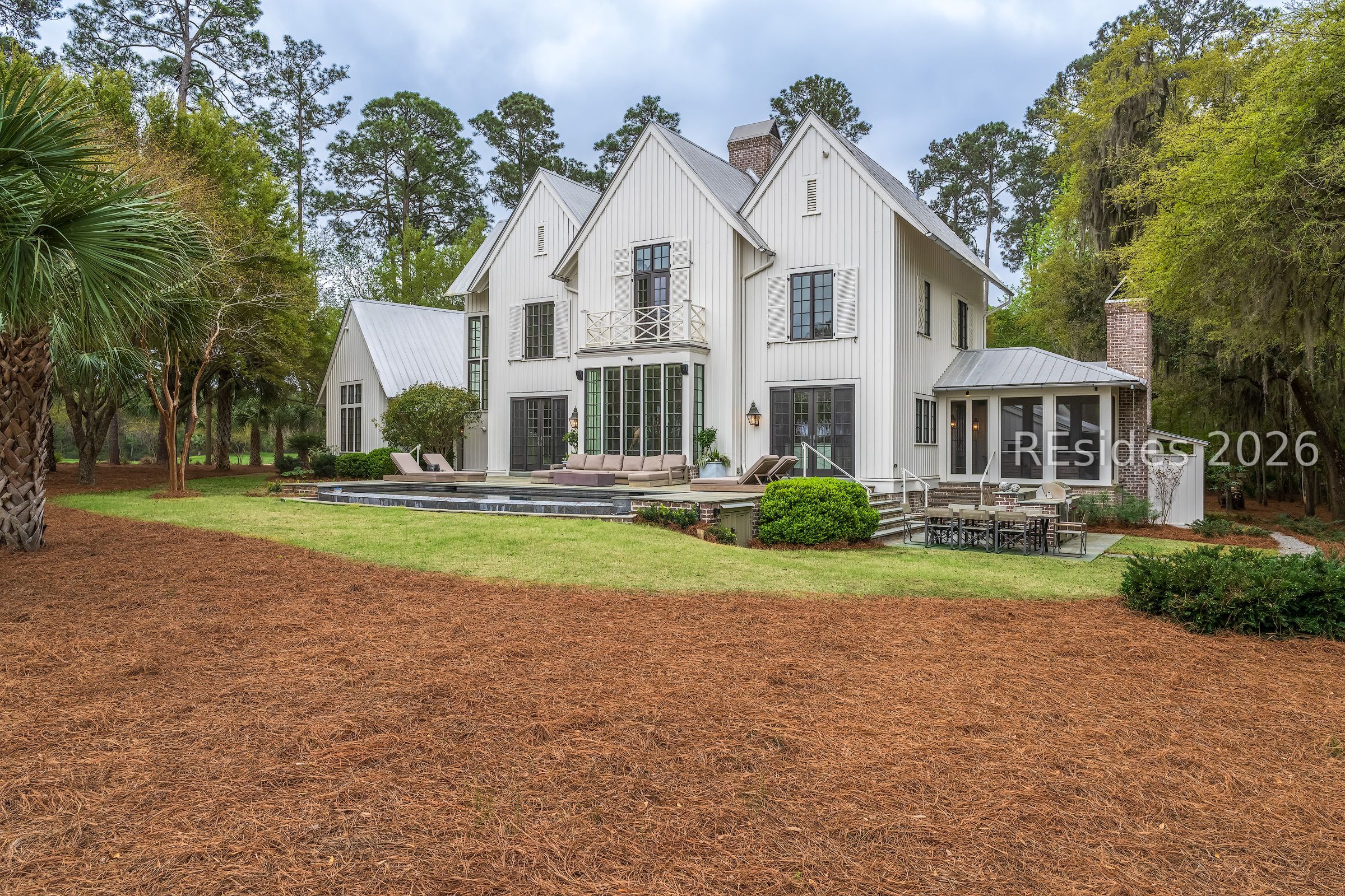 White multi-gabled house with a backyard pool, lounge seating, and outdoor dining area.