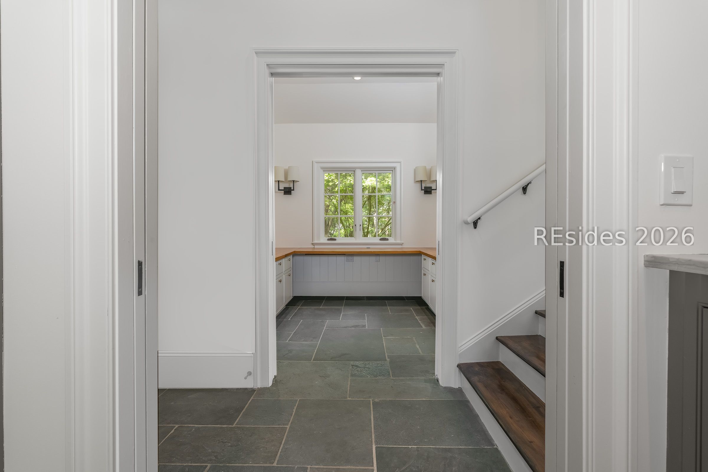 Hallway with slate flooring and a staircase, opening to a counter nook beneath a window.