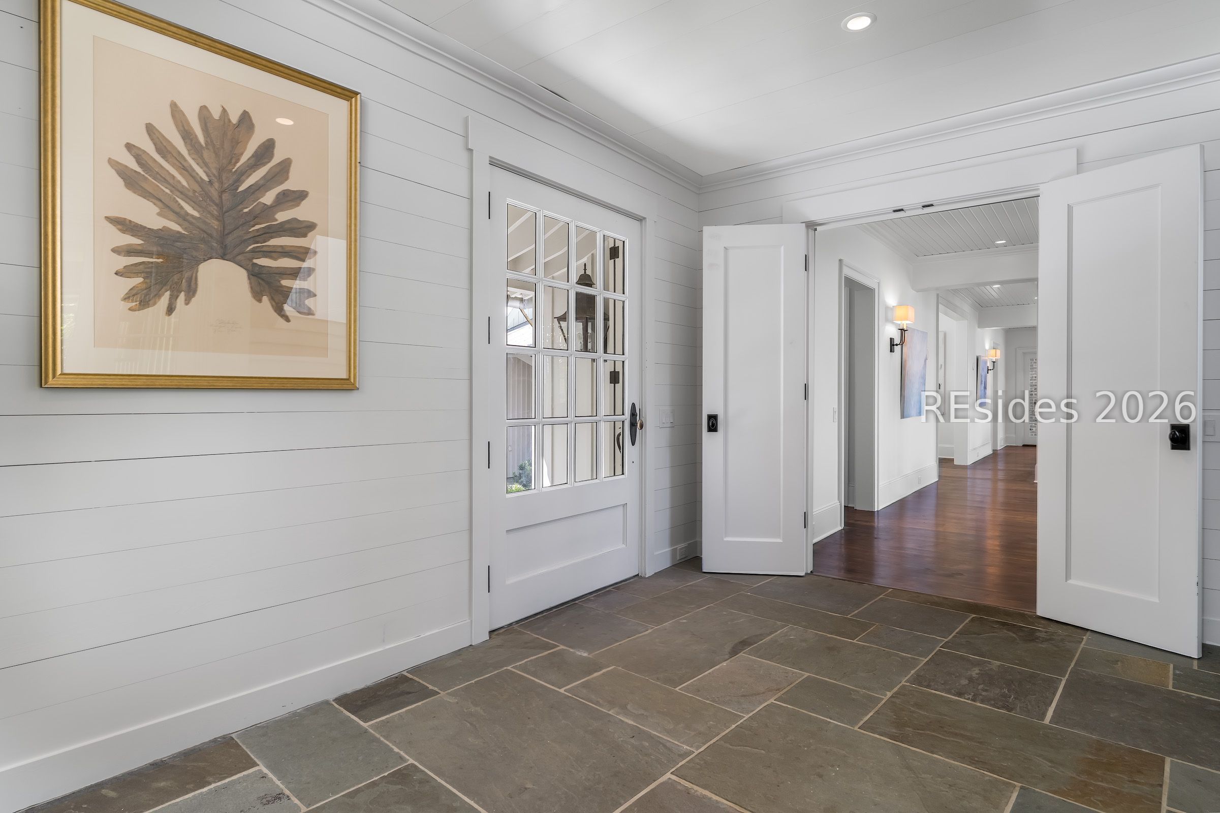 Entry foyer with dark stone tile, a glass-paneled front door, and open double doors to a wood-floored hall.