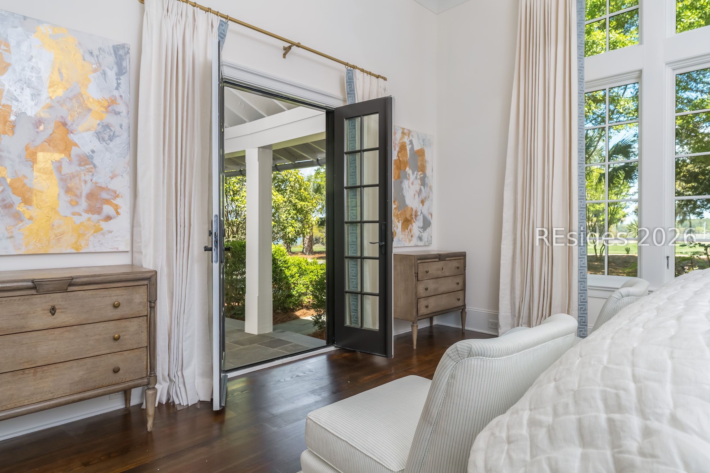 Furnished bedroom with open glass doors leading to a covered patio and leafy garden.