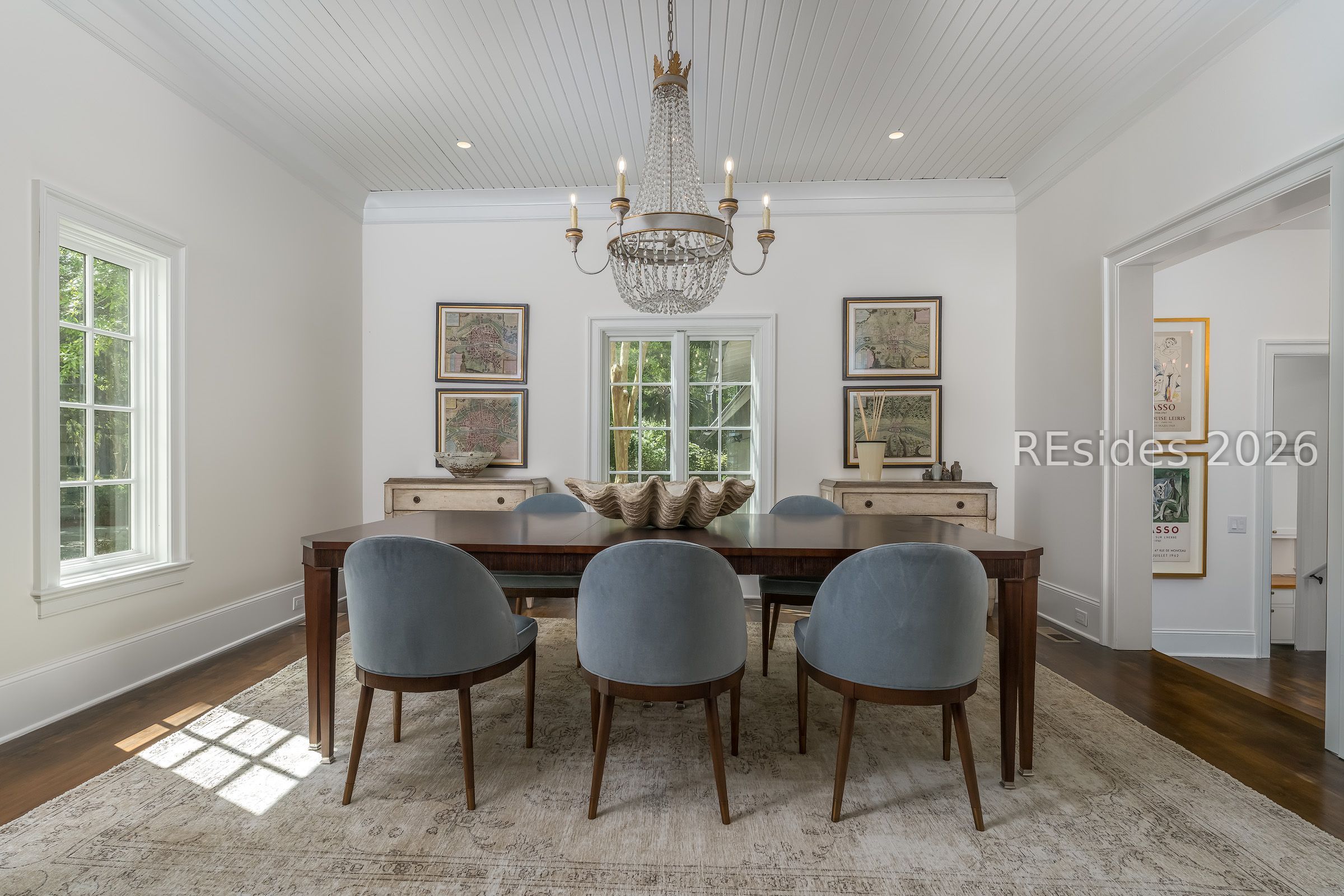 Dining room with a crystal chandelier, dark wood table, and blue-gray chairs beneath a paneled ceiling.
