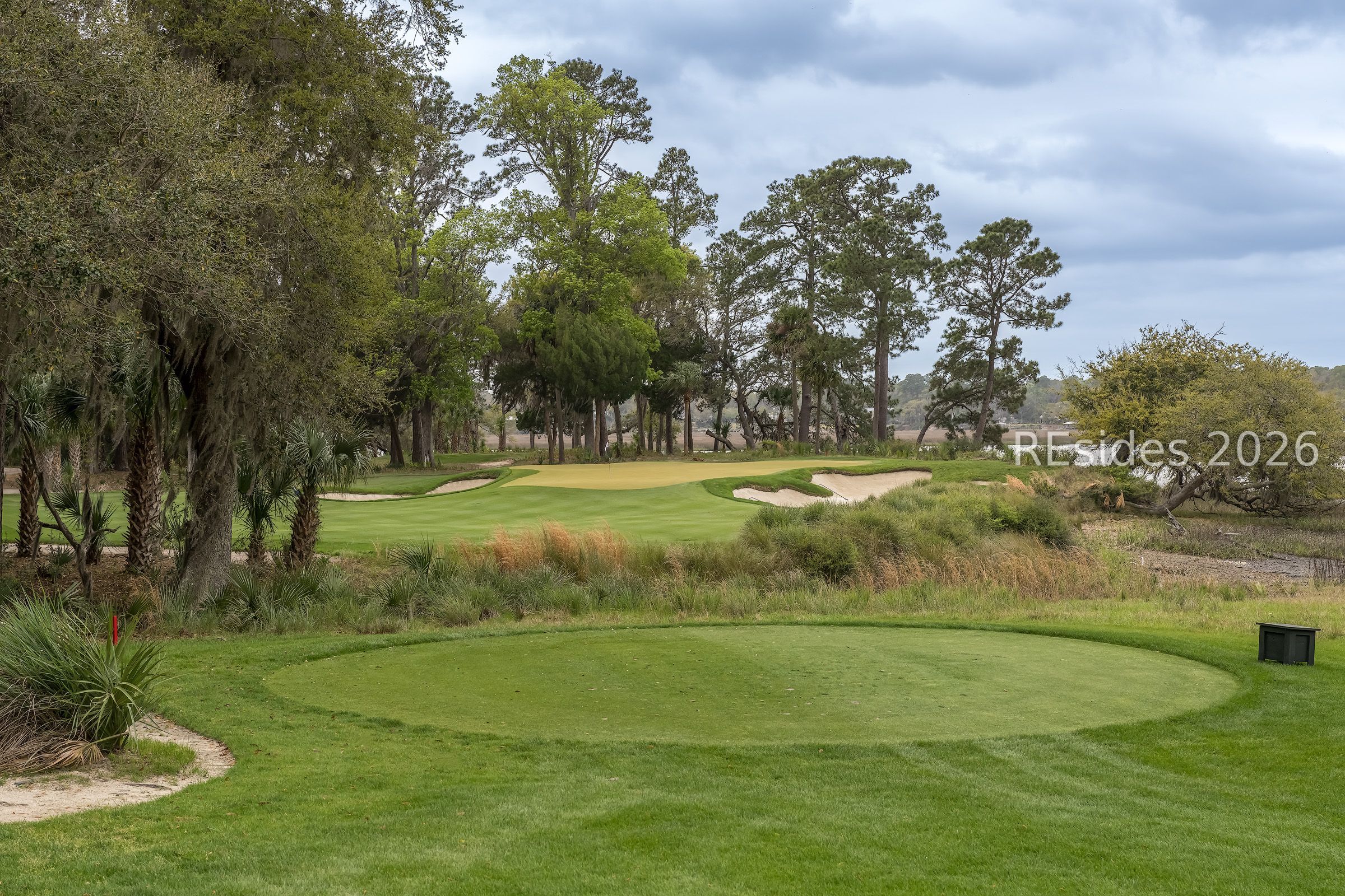 Golf course green with sand bunkers, mature trees, and native grasses.