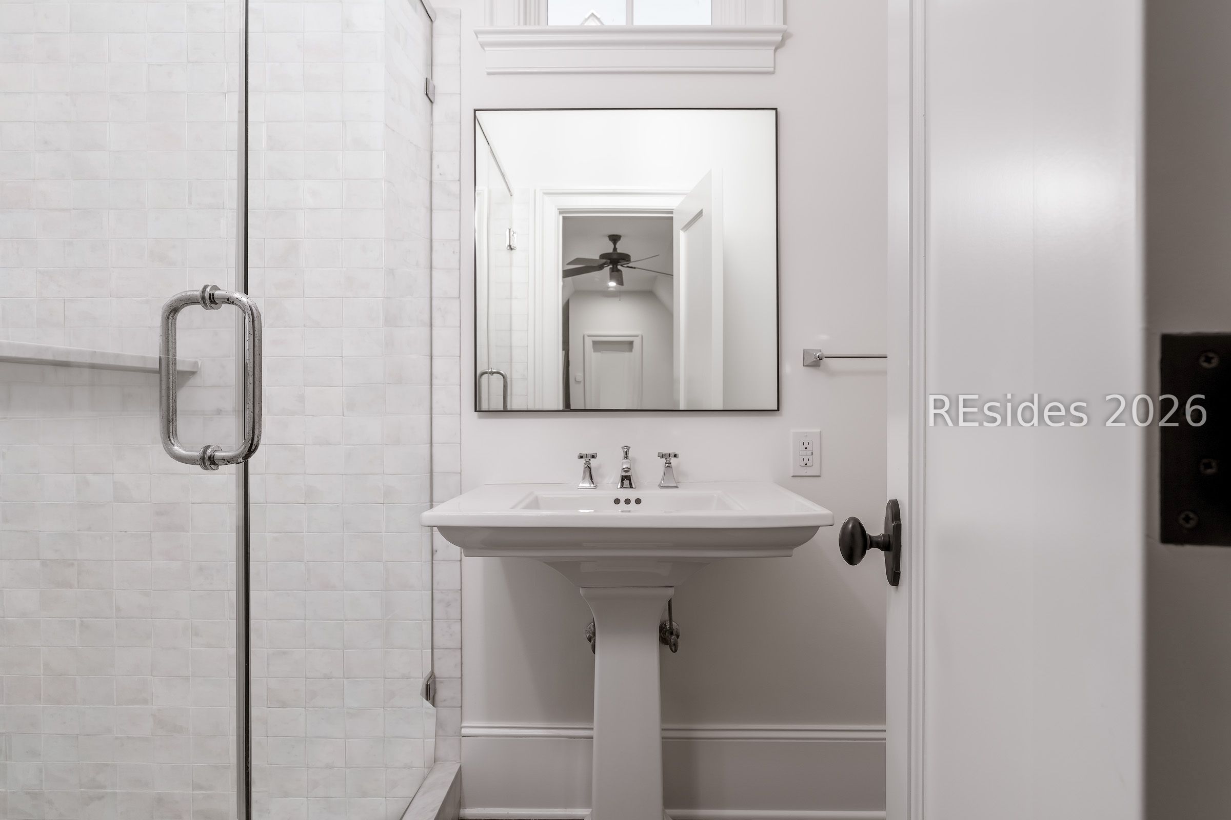 Bathroom with a white pedestal sink, tiled glass shower, and large mirror.