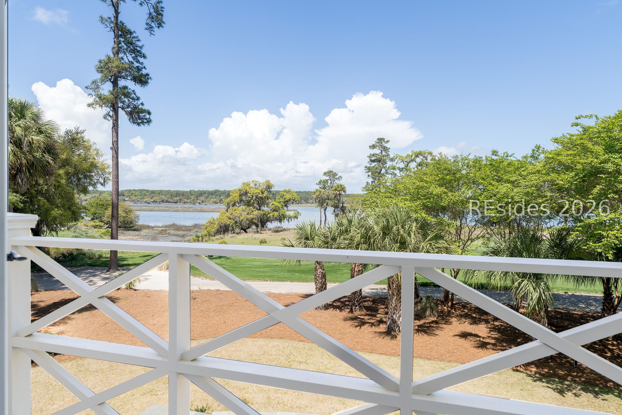 Porch view across a landscaped yard to a marshy waterway, framed by palms and trees.