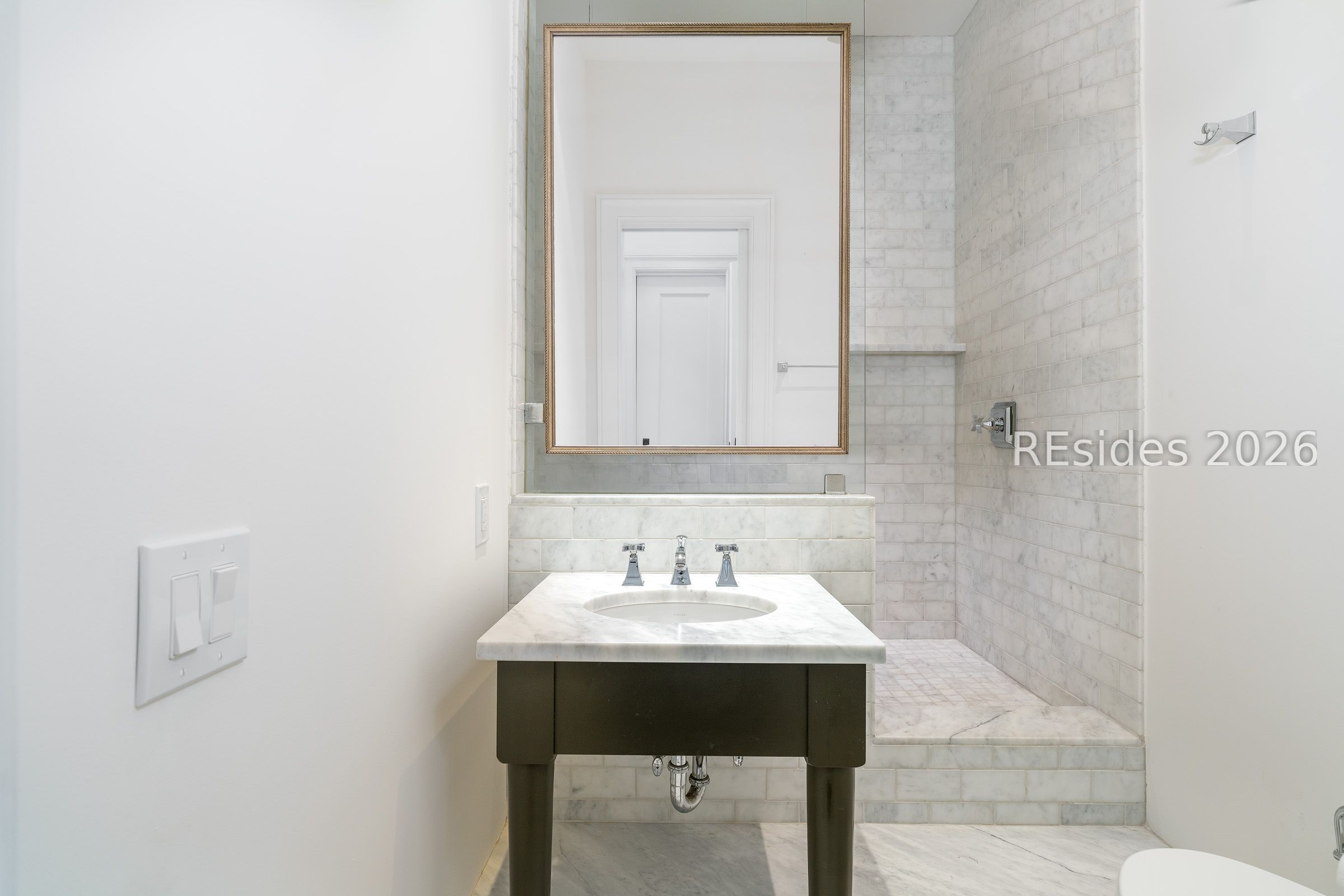 Bathroom with a marble-topped vanity, framed mirror, and marble-tiled walk-in shower.