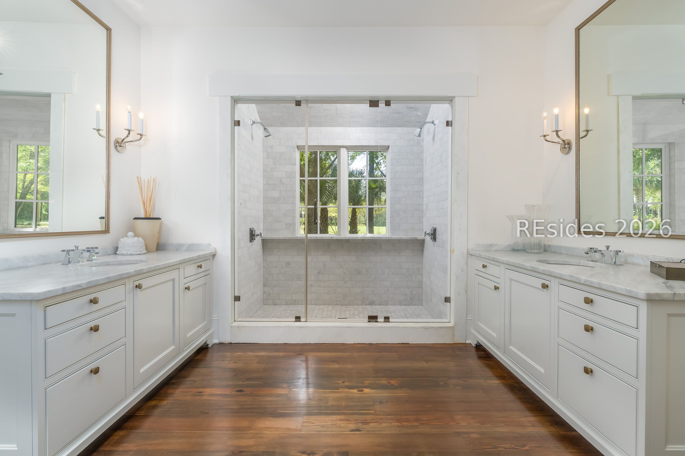Bathroom with a spacious tiled shower, dual marble-topped vanities, and dark wood flooring.