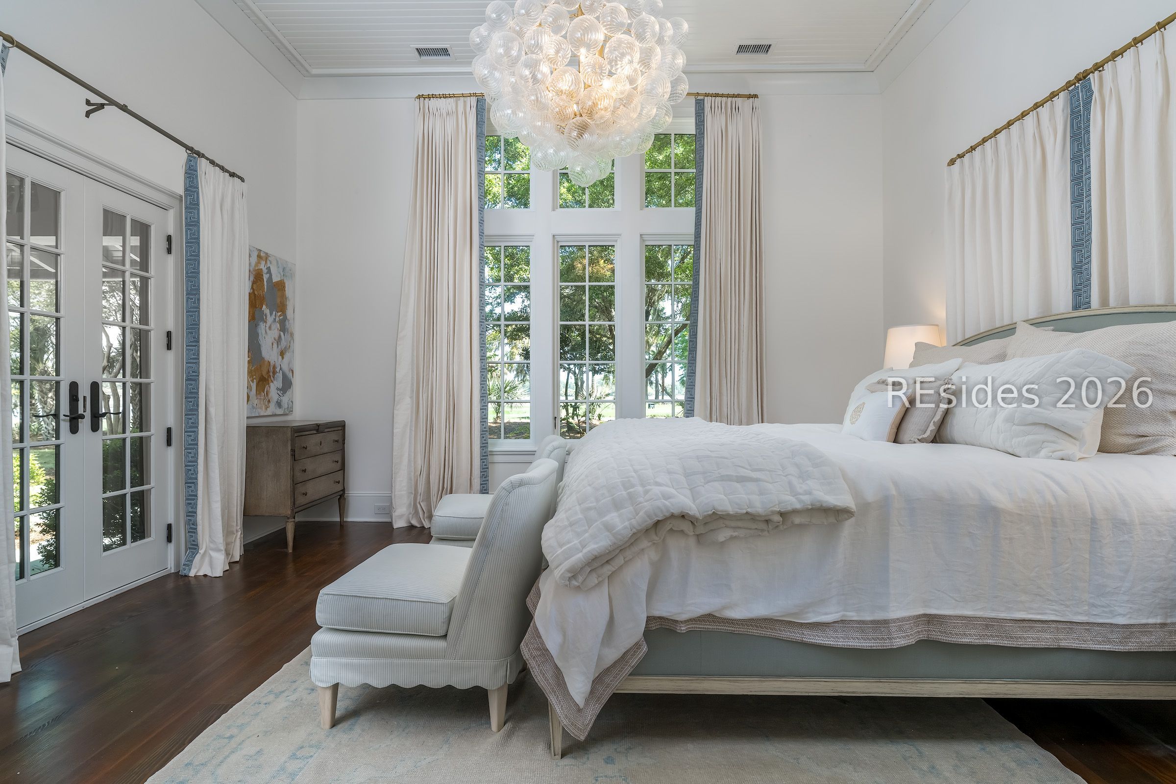 Bright bedroom with a large bed, tall windows, French doors, and a glass globe chandelier.