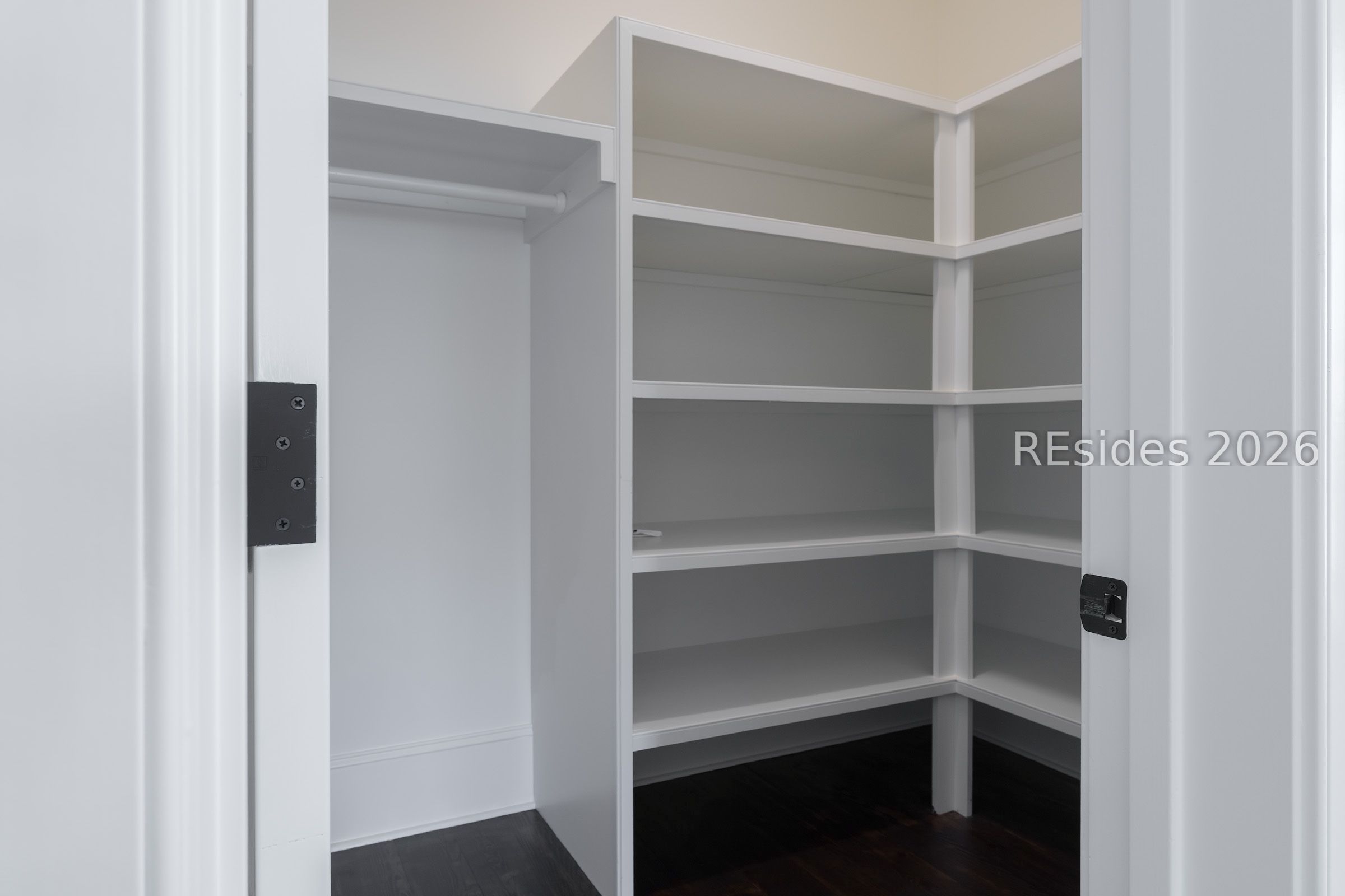 Walk-in closet with white built-in shelves, a hanging rod, and dark hardwood flooring.