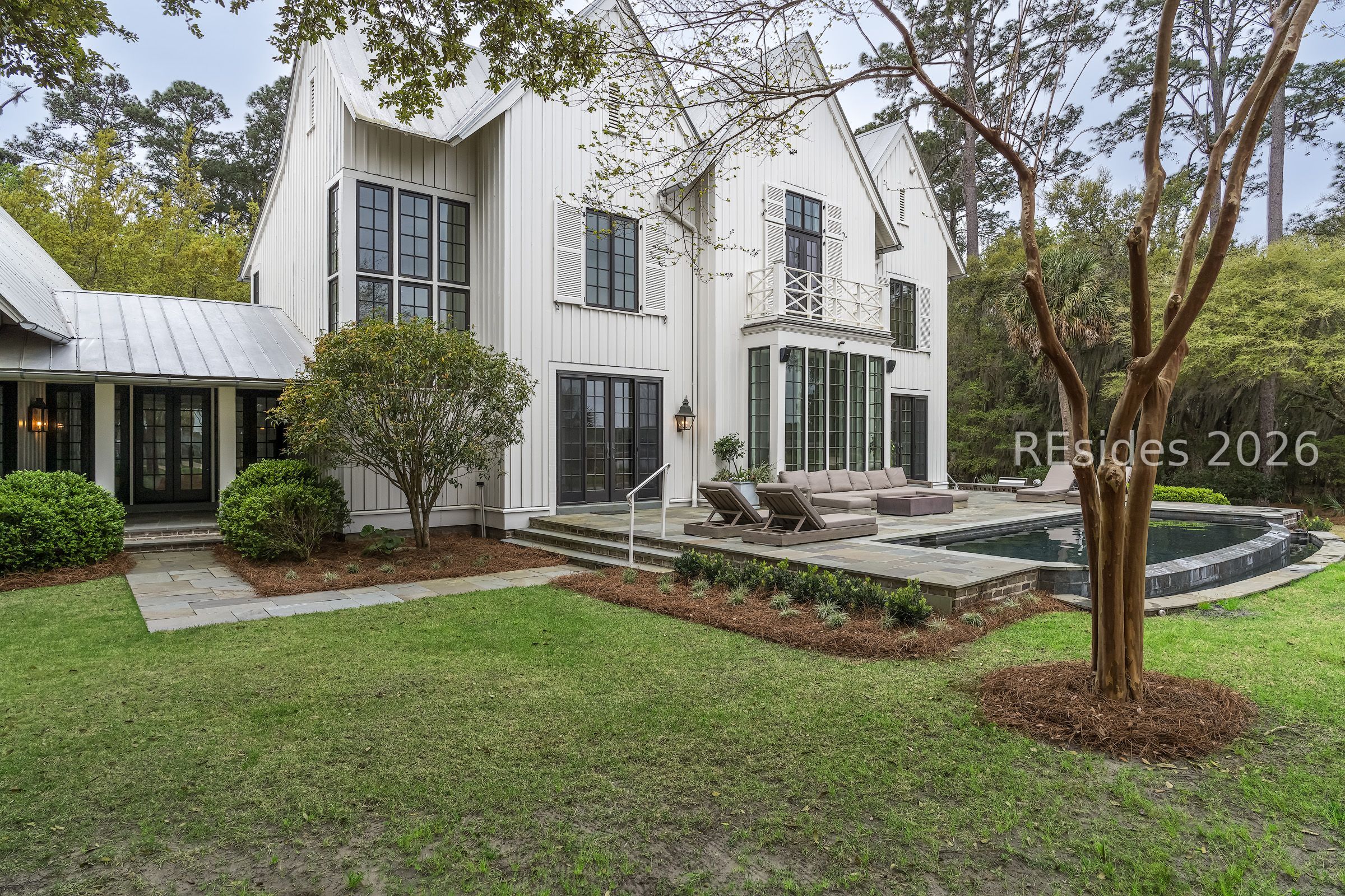 White house with dark-framed windows and a backyard pool bordered by a stone patio.