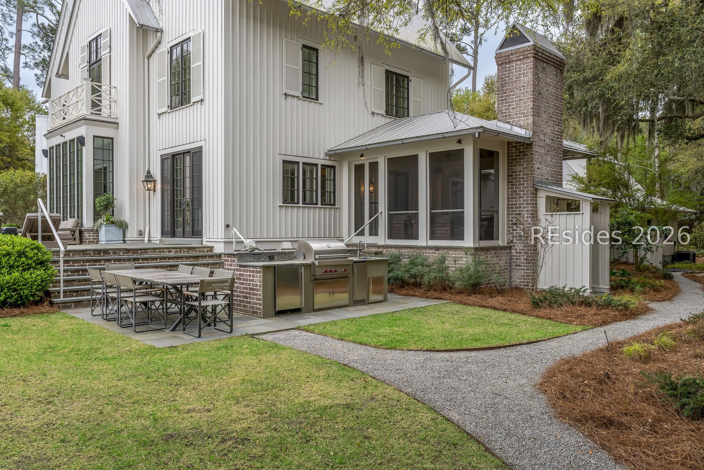 White-sided house with screened porch, brick chimney, and outdoor kitchen beside a furnished patio.