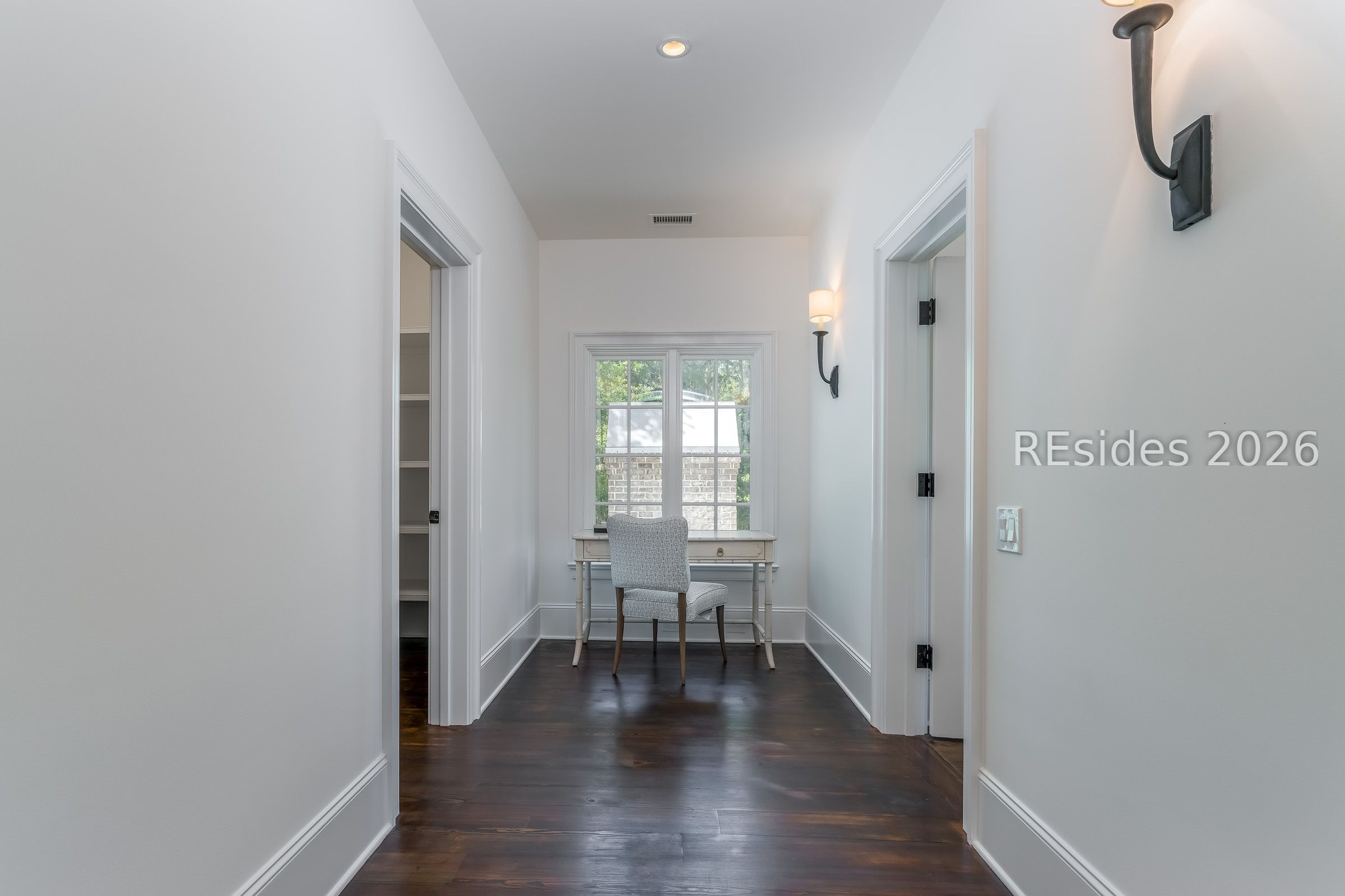 White hallway with dark hardwood floors and a furnished desk alcove beneath a window.