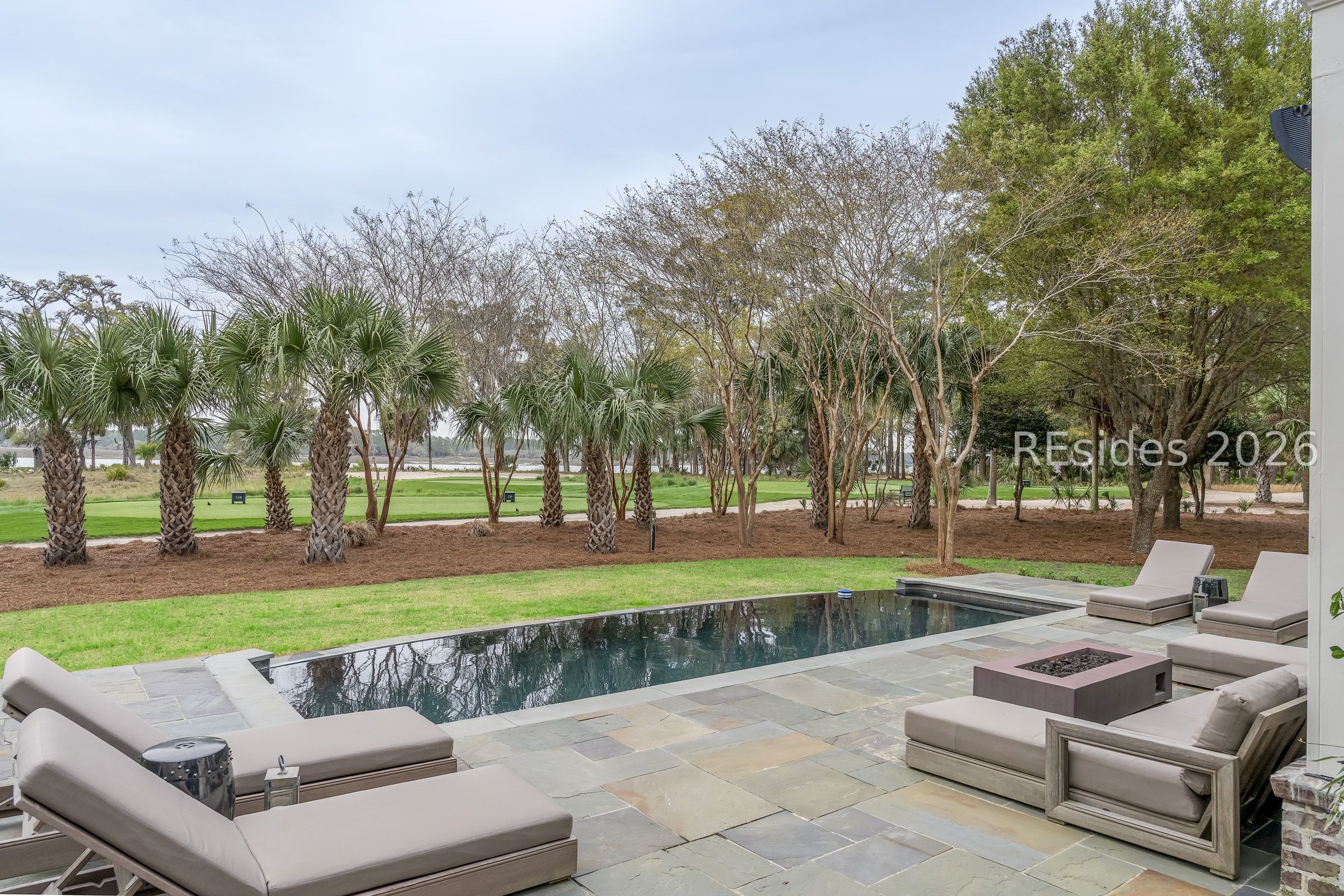 Pool terrace with stone paving, lounge chairs, and palms beside a grassy golf course and water.