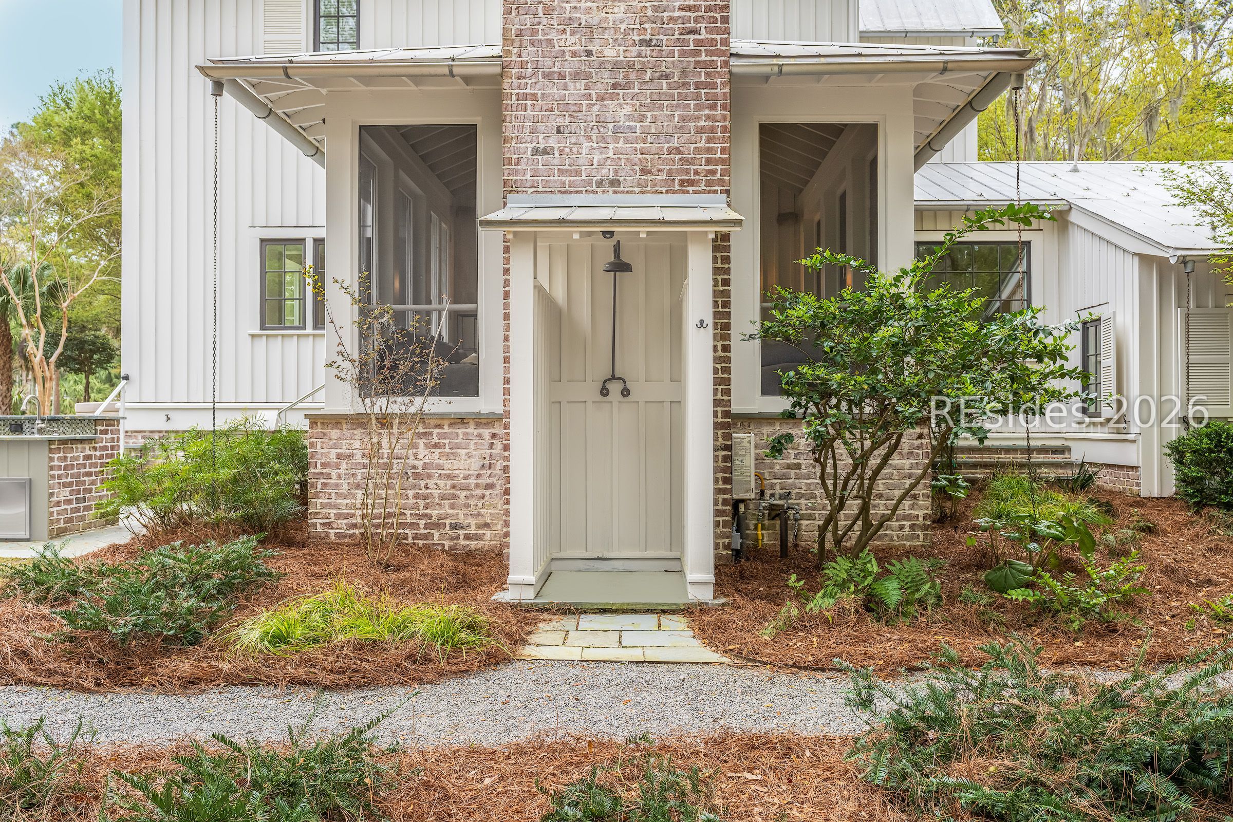 White-sided home with a brick chimney, covered entry porch, and landscaped garden beds.