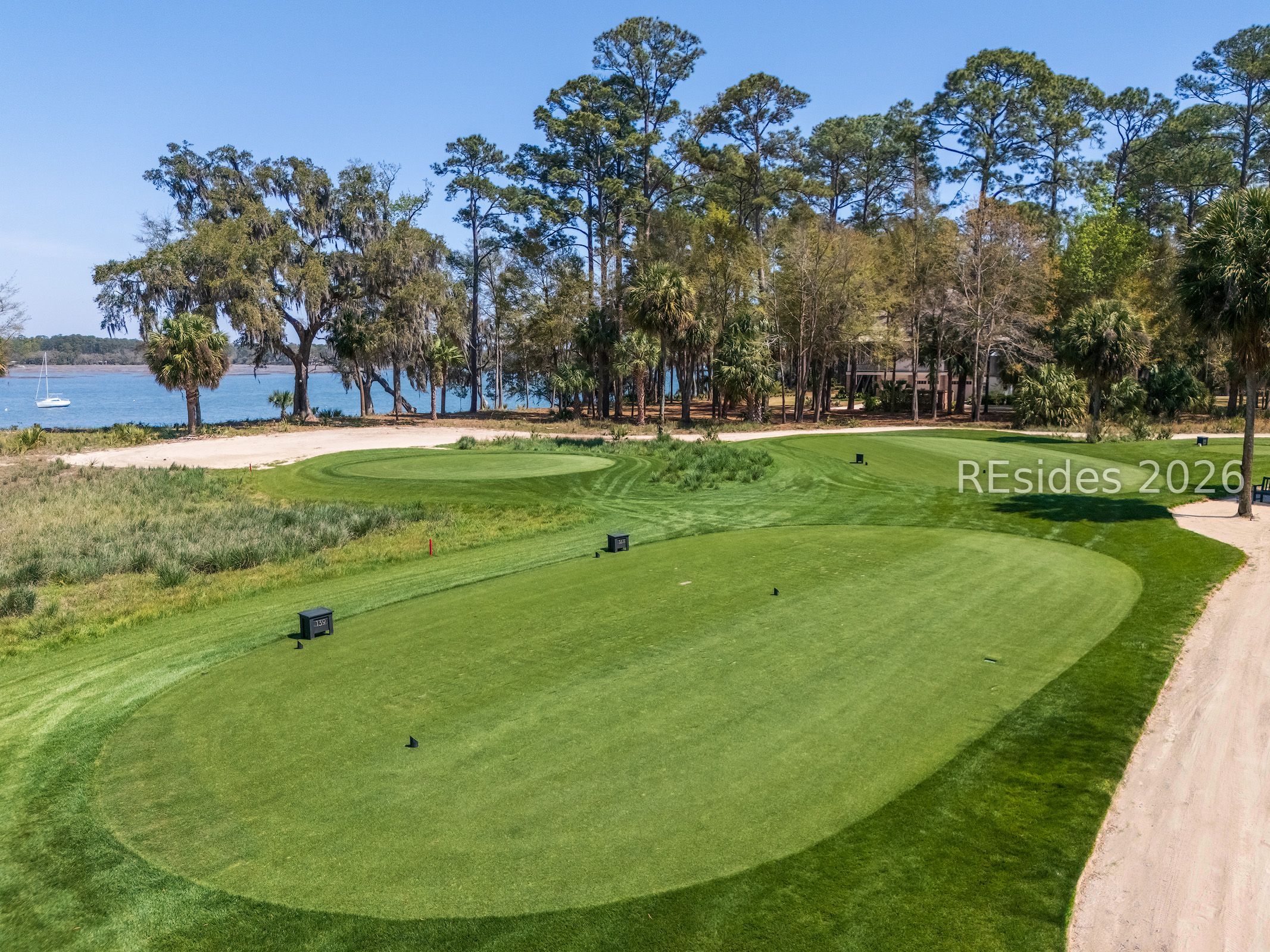 Golf course tee box beside the water, framed by palms and marsh grass.