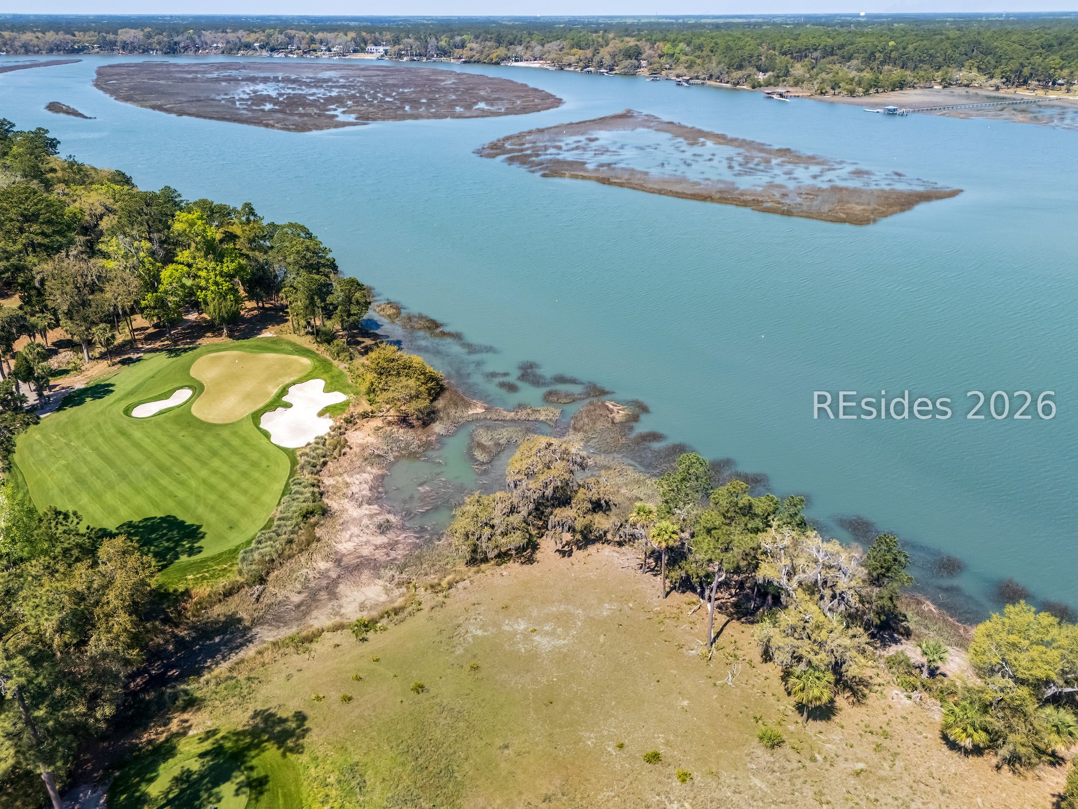 Aerial coastal property beside a tidal estuary, with marshland and a golf hole with sand bunkers.