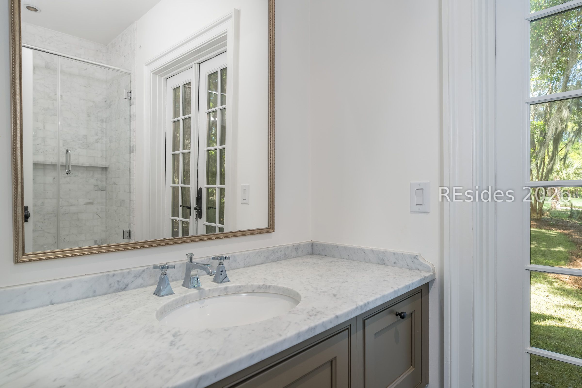 Bathroom vanity with a marble counter, chrome faucet, framed mirror, and glass-paneled door.