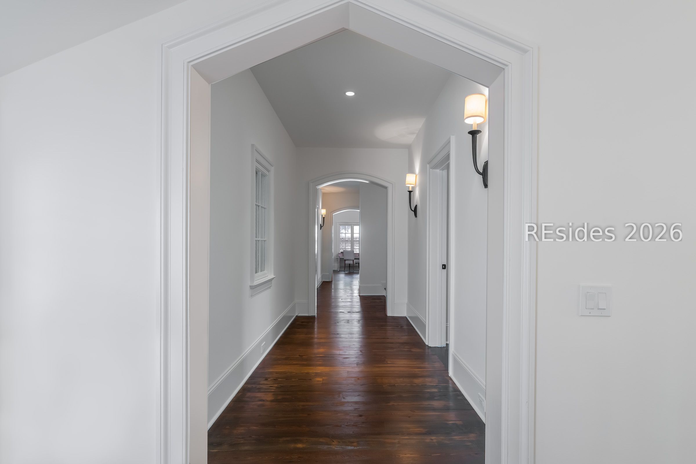 Interior hallway with dark hardwood floors, arched doorways, and wall sconces.