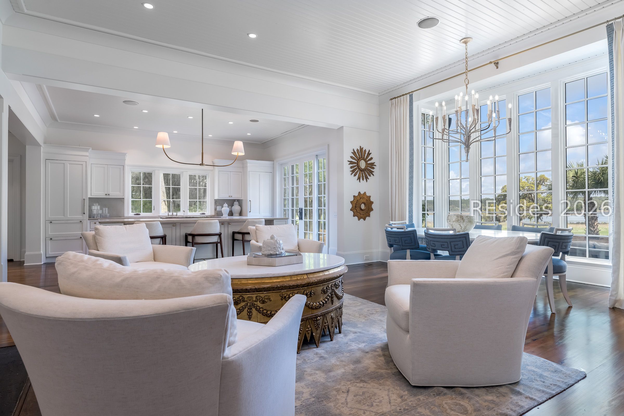 Open-plan living room and kitchen with pale seating, tall grid windows, and a dining table.